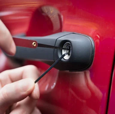 Red car with a driver-side door lock being opened by a professional lockout technician.