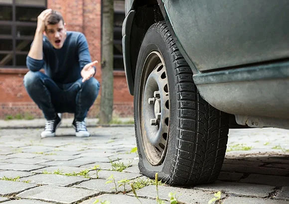 Man crouching beside a car with a flat tire in Citrus Heights, CA, showcasing emergency tire change services.
