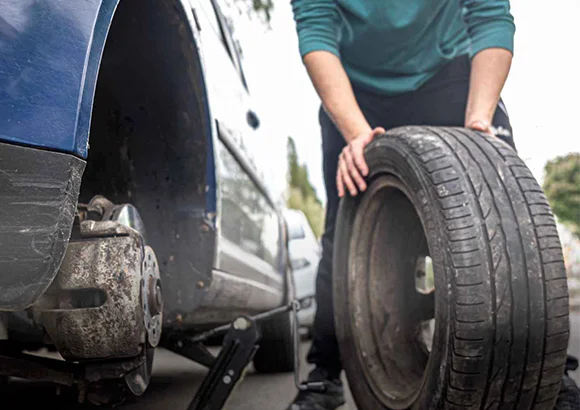 Professional technician using tools to change a flat car tire on the roadside in Rocklin, CA, demonstrating reliable tire change services.